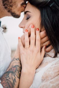 a man and woman kissing each other with tattoos on their arms, both wearing rings