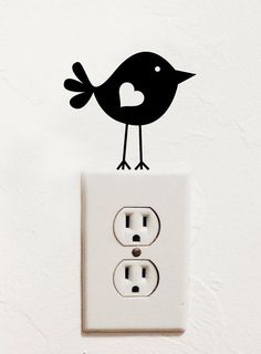 a black bird sitting on top of a white electrical outlet with a heart cut out of it's side