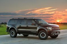 a black truck is parked on the side of the road at sunset or dawn with grass and trees in the background