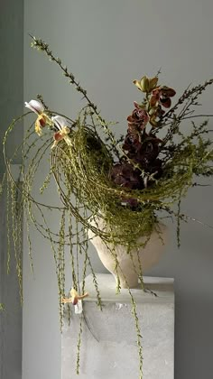 an arrangement of flowers in a white vase on a pedestal with greenery growing out of it