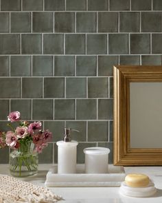 a bathroom counter with soap, toothbrush and flowers in a vase next to a mirror