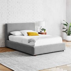 a bed sitting on top of a wooden floor next to a white brick wall