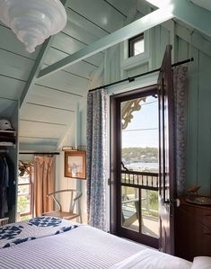 a bedroom with an open door leading to a balcony overlooking the water and trees in the distance