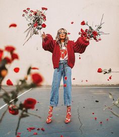 a woman standing in front of flowers holding her arms out with both hands and looking at the camera