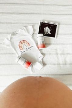 a pregnant woman laying in bed next to some skin care products on top of her stomach