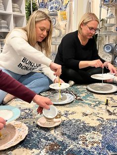 three women sitting at a table with plates and bowls in front of them on the floor