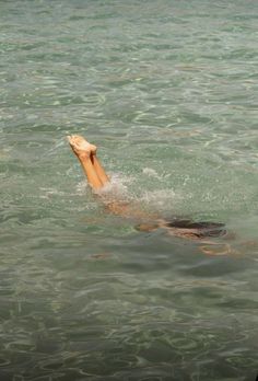 a man swimming in the ocean with his feet up and head above water's surface