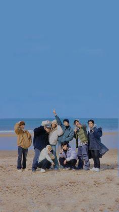 a group of people standing on top of a sandy beach next to the ocean under a blue sky