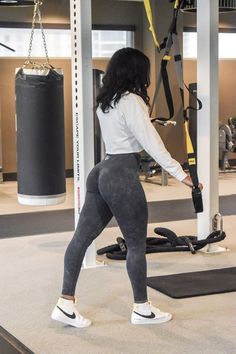 a woman in grey leggings and white shirt doing exercises on a gym machine