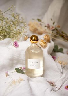 a bottle of perfume sitting on top of a white cloth next to flowers and plants