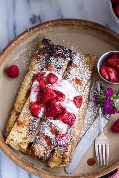 french toast topped with strawberries and powdered sugar on a plate next to berries