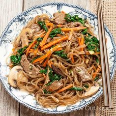 a plate full of noodles and vegetables with chopsticks next to it on a wooden table