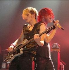 two people on stage with guitars and microphones in their hands, one holding a guitar