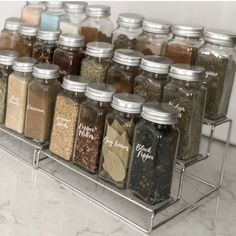 an assortment of spices and seasonings in glass jars on a metal shelf with clear shelves