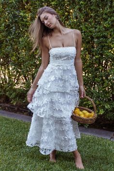 a woman in a white dress holding a basket full of lemons on the grass