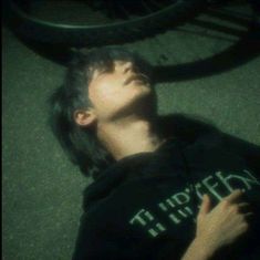 a young man laying on the ground with his head up in front of a bike tire