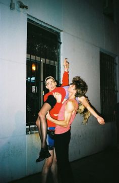 two people standing on the side of a building with their arms around each other and one person holding another