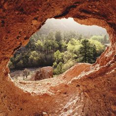 a hole in the side of a mountain filled with trees