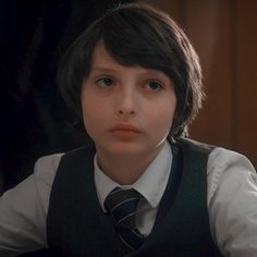 a young boy wearing a vest and tie talking to someone