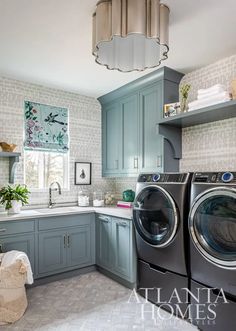 a washer and dryer in a kitchen with blue cabinets, white tile flooring and a chandelier