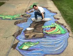 a man kneeling down next to a chalk drawing on the sidewalk with crocodiles and fish