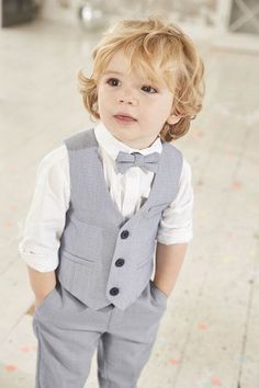 a little boy wearing a gray suit and bow tie standing on the floor with his hands in his pockets