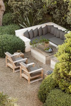 an outdoor seating area with couches and tables surrounded by shrubbery, shrubs and trees