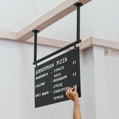 a person writing on a black sign in front of a white wall and wooden beams