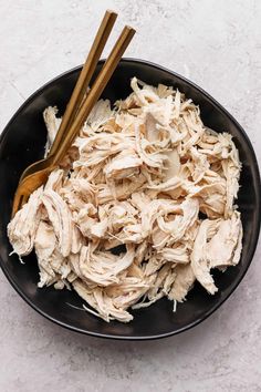 a black bowl filled with shredded chicken and two wooden spoons