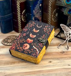 a small notebook covered in black and orange designs on a wooden table next to other books