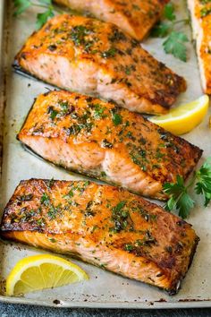 three salmon fillets on a baking sheet with lemon wedges and parsley sprigs