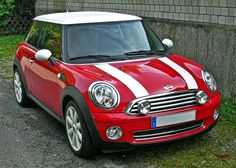 a small red and white car parked in front of a stone wall next to grass