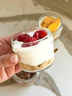 a person holding a small glass jar filled with desserts and fruit on the side