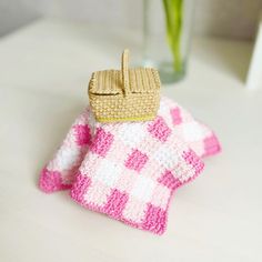 a pink and white knitted dishcloth with a basket on it sitting next to a vase