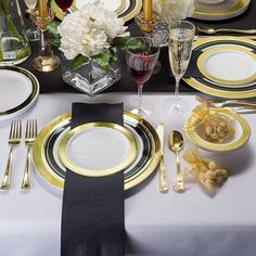 the table is set with black and gold plates, silverware, and white flowers