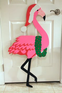 a pink flamingo standing in front of a door with a santa hat on it's head