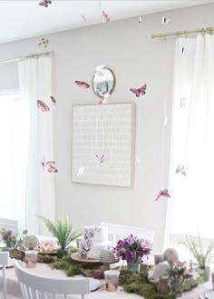 a dining room table with white chairs and pink butterflies on the wall above it, surrounded by greenery