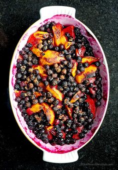 a bowl filled with blueberries and peaches on top of a black countertop