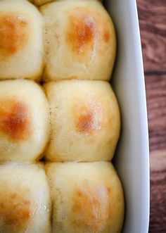 several rolls in a white dish on a wooden table