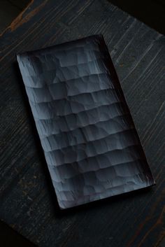 a wooden table topped with a black tray covered in dark colored paper next to a cup of coffee