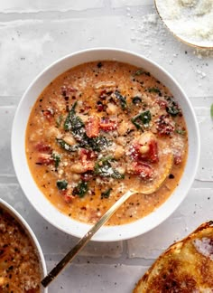 two bowls filled with soup next to bread on a white counter top and one bowl is full of soup