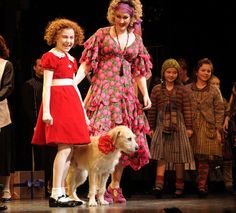 two women and a dog on stage with other people in the background wearing red dresses