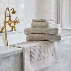 a stack of towels sitting on top of a bath tub next to a golden faucet