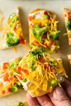 a person holding a piece of broccoli and cheese pizza