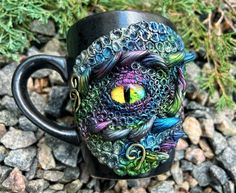 a black coffee mug with an eye painted on the side and some rocks around it