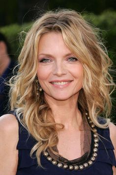 a woman with blonde hair and blue eyes smiles at the camera while wearing a black dress