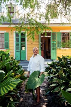 an older man standing in front of a yellow house with green shutters on the windows