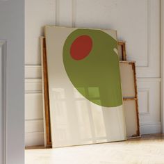 a green and red painting sitting on top of a hard wood floor next to a white wall