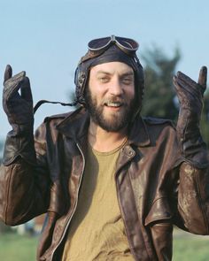 a man wearing a leather jacket and aviator's hat with his hands in the air