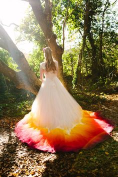 a woman in a white dress standing next to a tree with red, yellow and orange dye on it